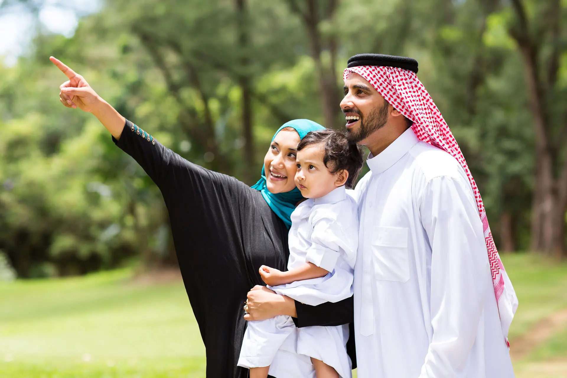 Happy Saudi family with the the mother and father holding the child and the mother is pointing happily to the horizon
